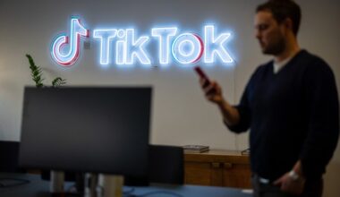 A man looks at his phone while walking past a neon TikTok logo on the wall inside the TikTok UK office.