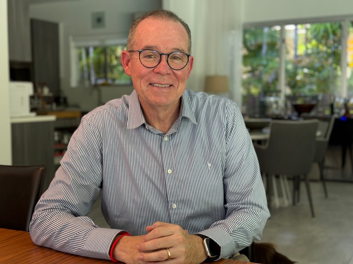 A man in a striped shirt and glasses sits at a kitchen table. 