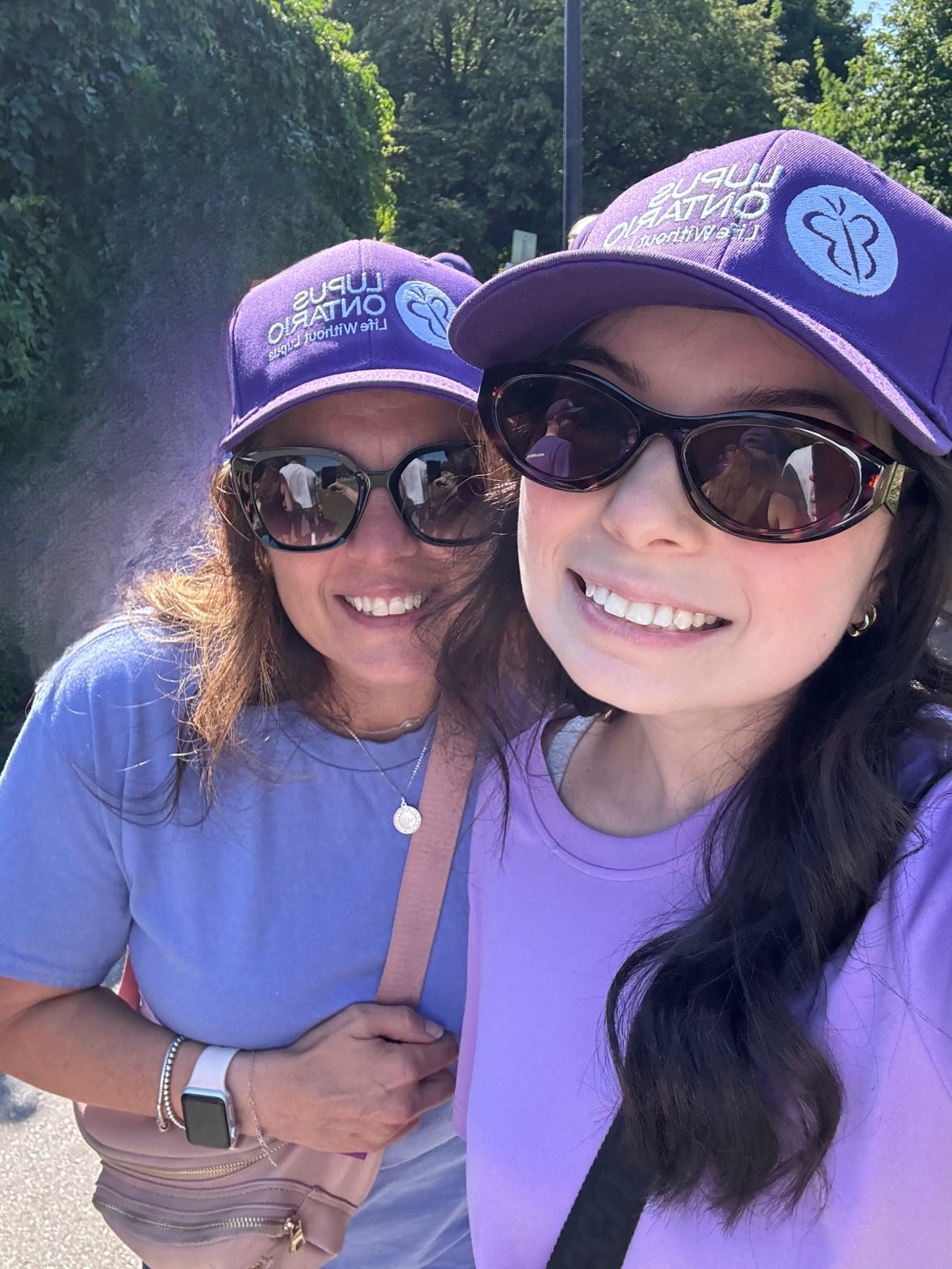 Two smiling women pose for a selfie. They’re both wearing purple caps and shirts. 