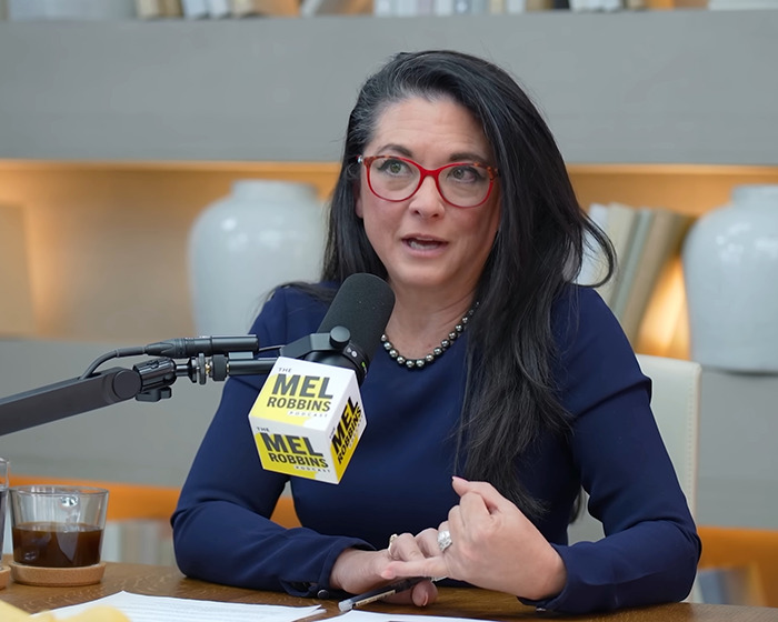 Woman with red glasses speaking into a microphone during a podcast about the push-ups challenge changing a woman’s life.