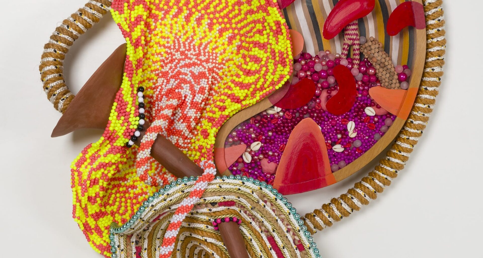 an abstract yellow and magenta sculpture by Maria Nepomuceno made of beads, resin, wood, and string