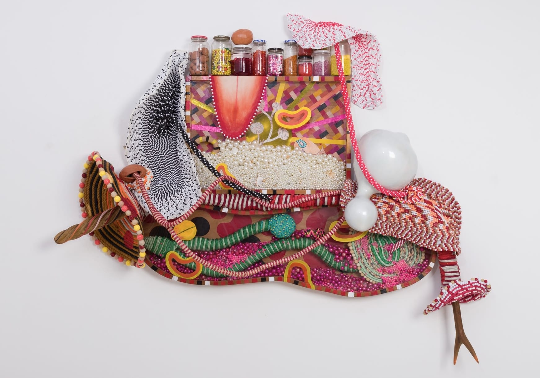an abstract wall sculpture by Maria Nepomuceno made of beads, jars, resin, wood, and string
