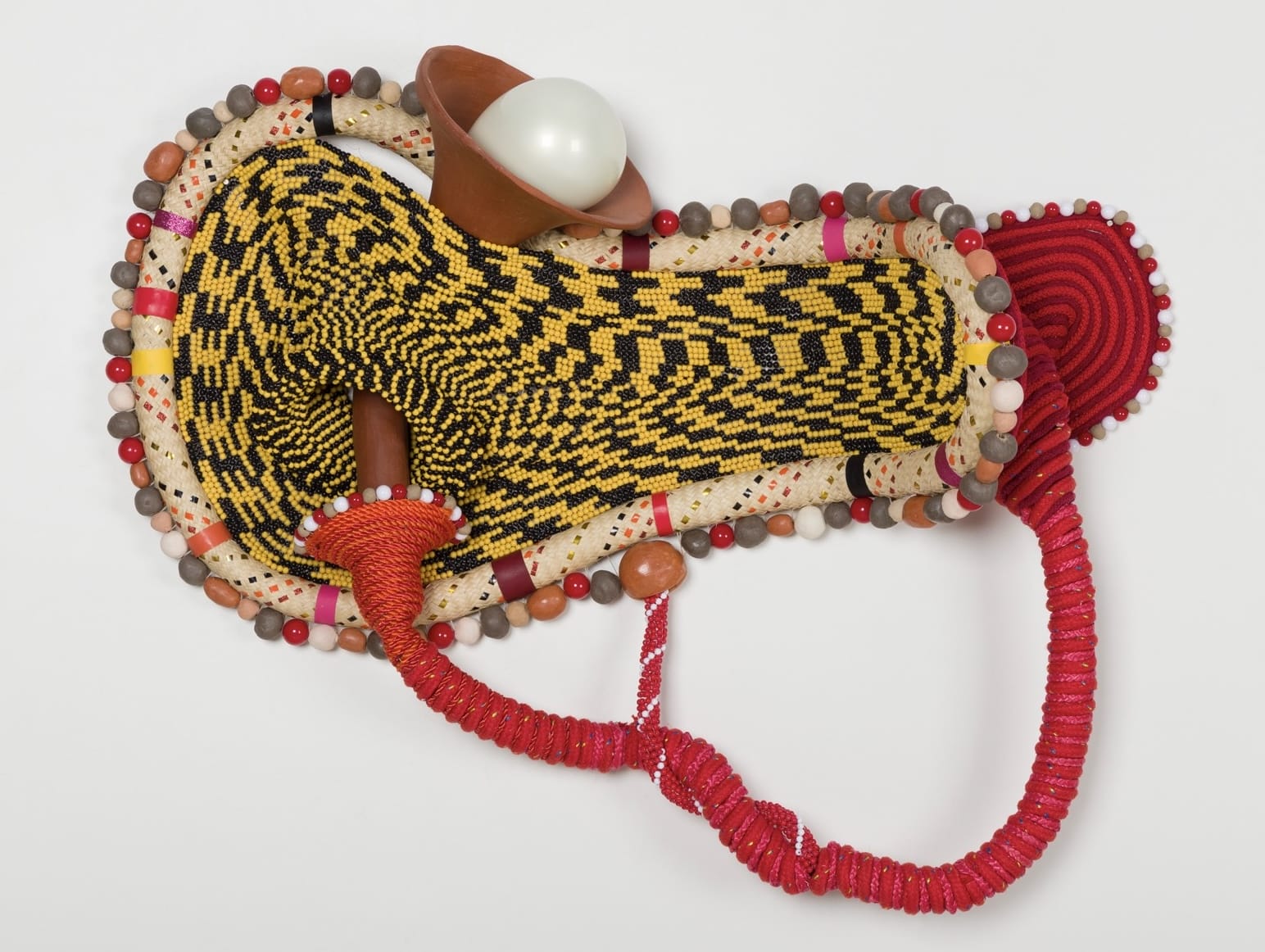 an abstract yellow and red sculpture by Maria Nepomuceno made of beads, resin, wood, and string
