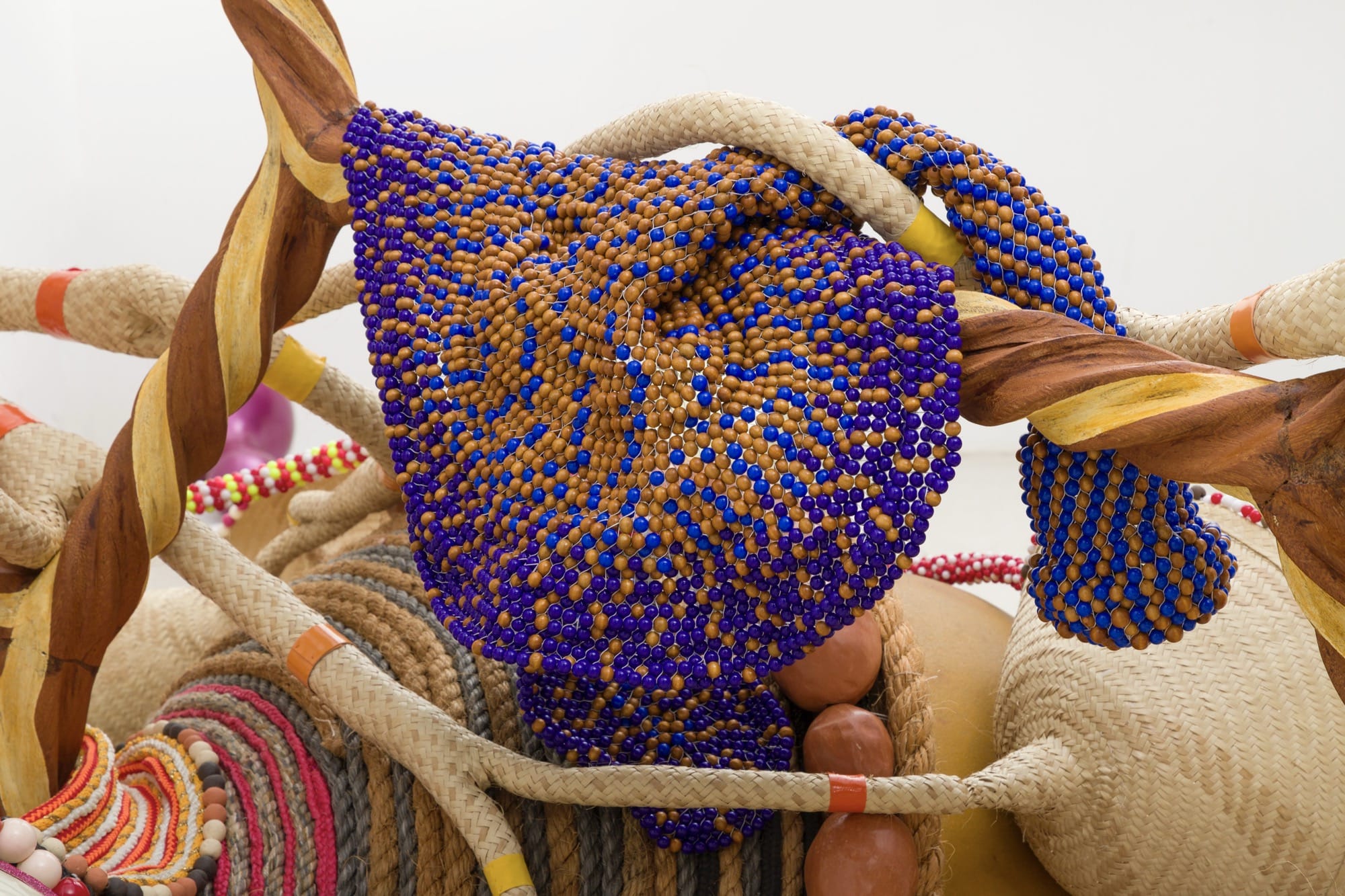 a detail of an abstract sculpture by Maria Nepomuceno, made with beads, wood, straw, resin, and other materials