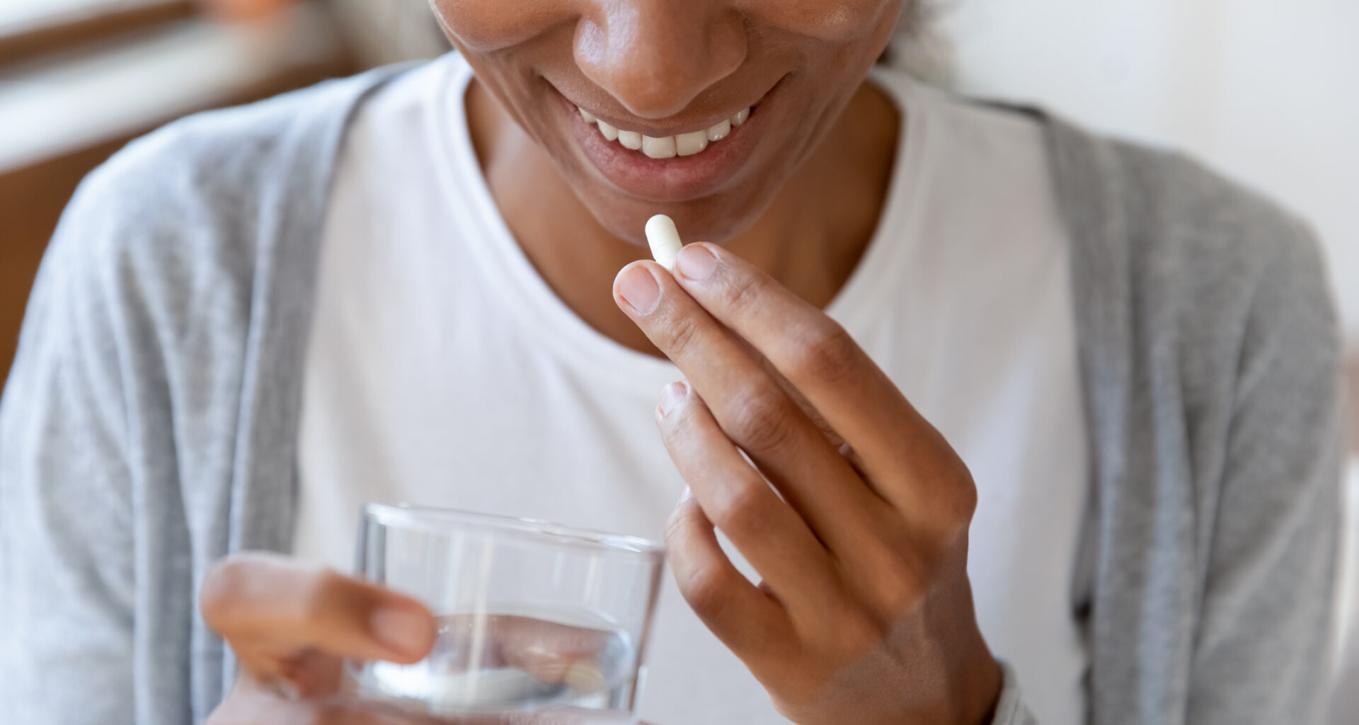 Woman holding a glass of water brings a pill towards her lips