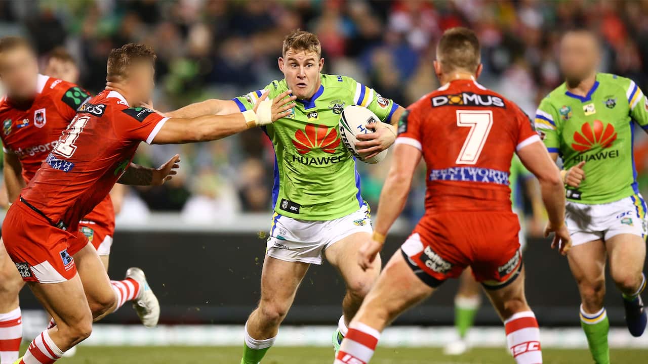 A rugby league player in a lime-green jumper holds the ball as he runs towards other players in red uniforms 