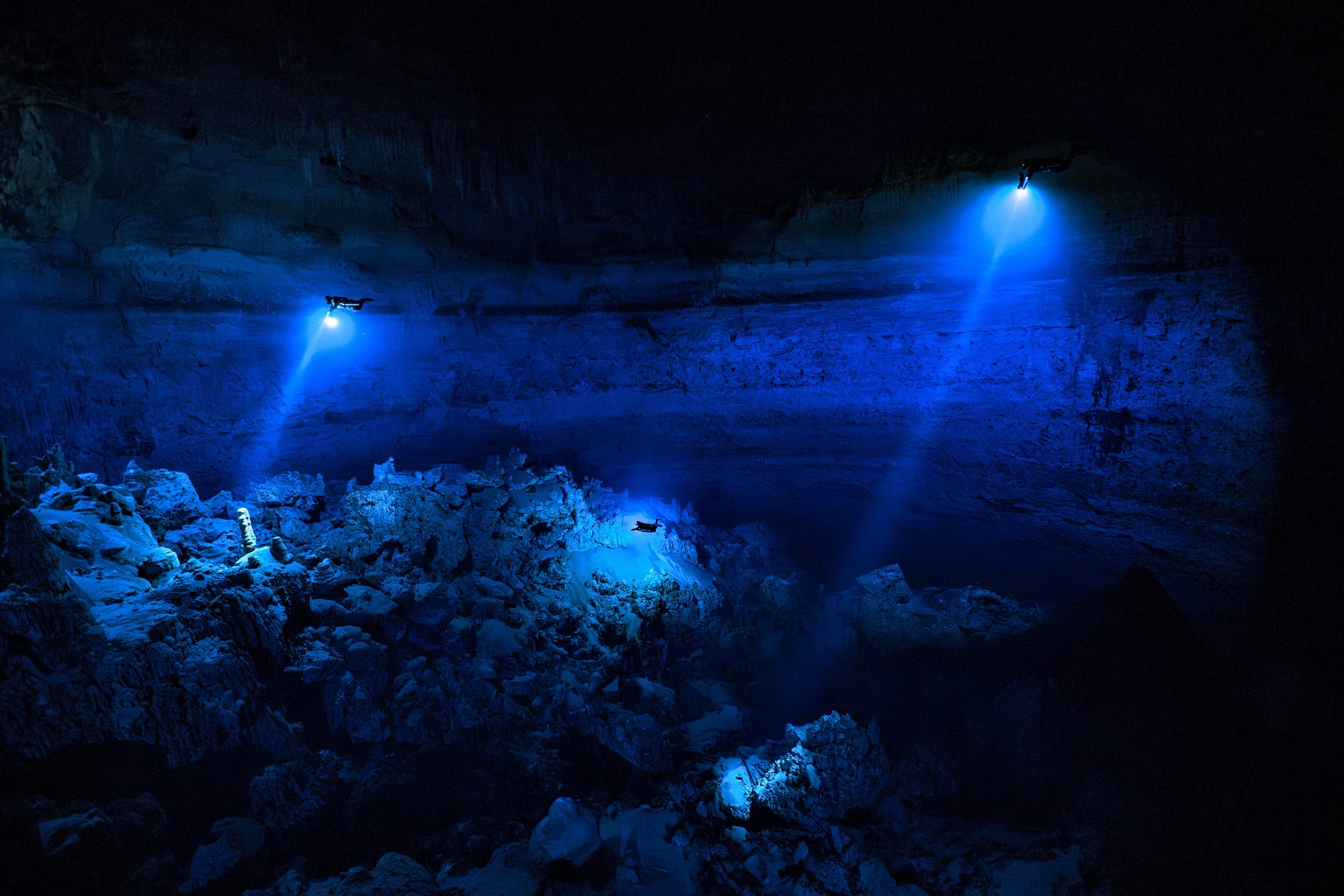two divers shine lights into a vast underwater cave