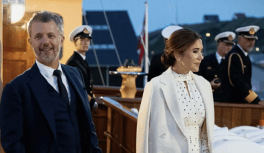 Queen Mary wearing a white polka dot dress and King Frederik in a suit standing on the royal yacht