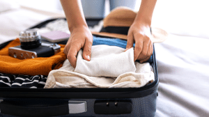 Someone packing a suitcase with clothes, a hat, and a camera.