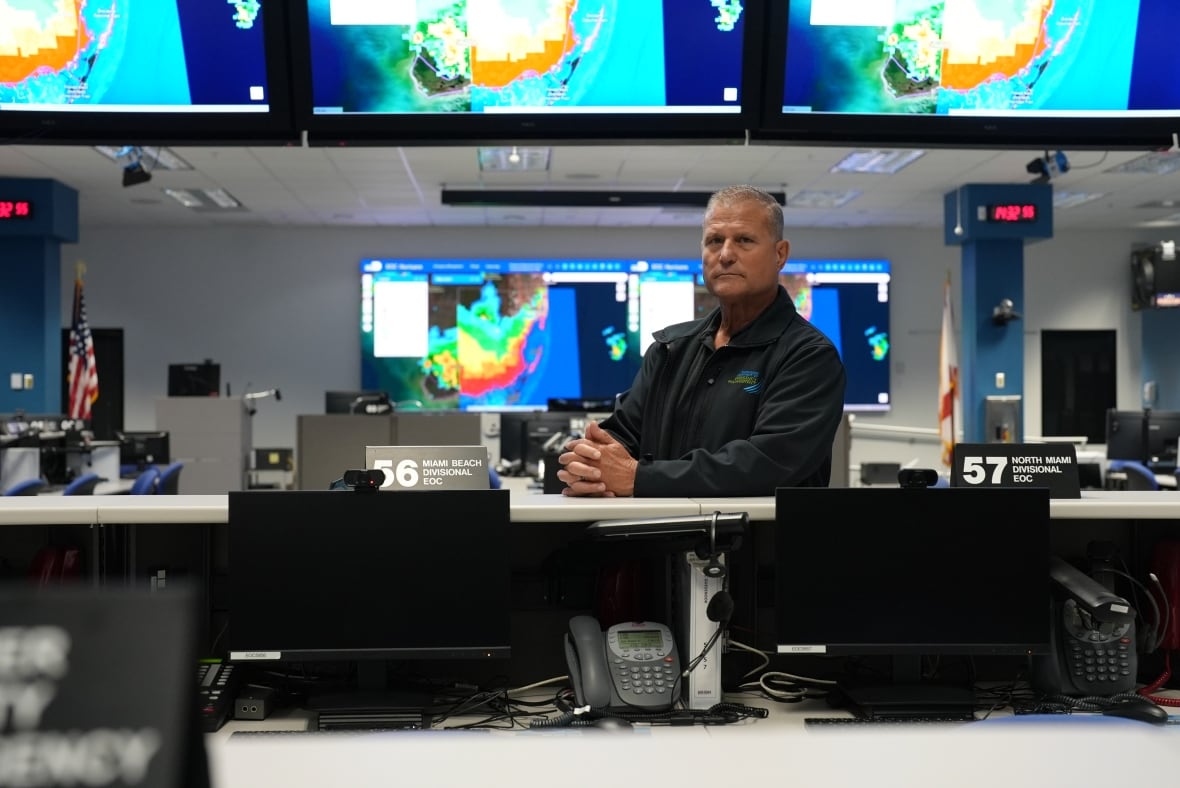 A man sits at a desk surrounded by TV monitors.