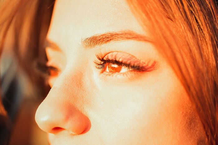 Close-up of a person's eye and nose illuminated by warm light showing details of the human body features.