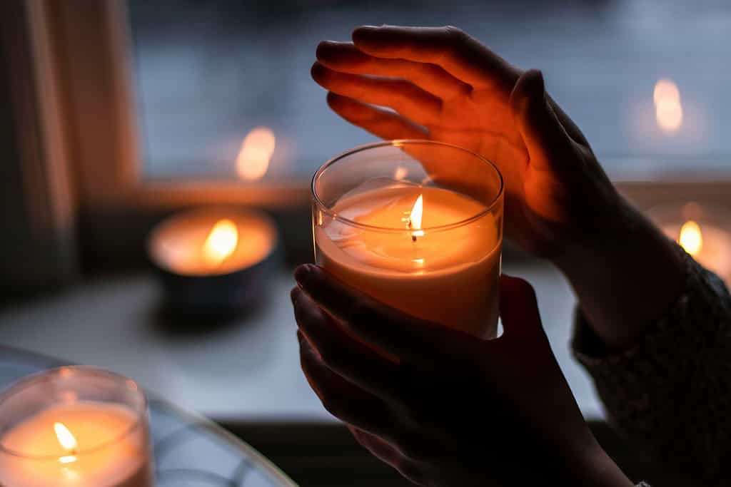 someone holding a scented candle inside a room with other candles around