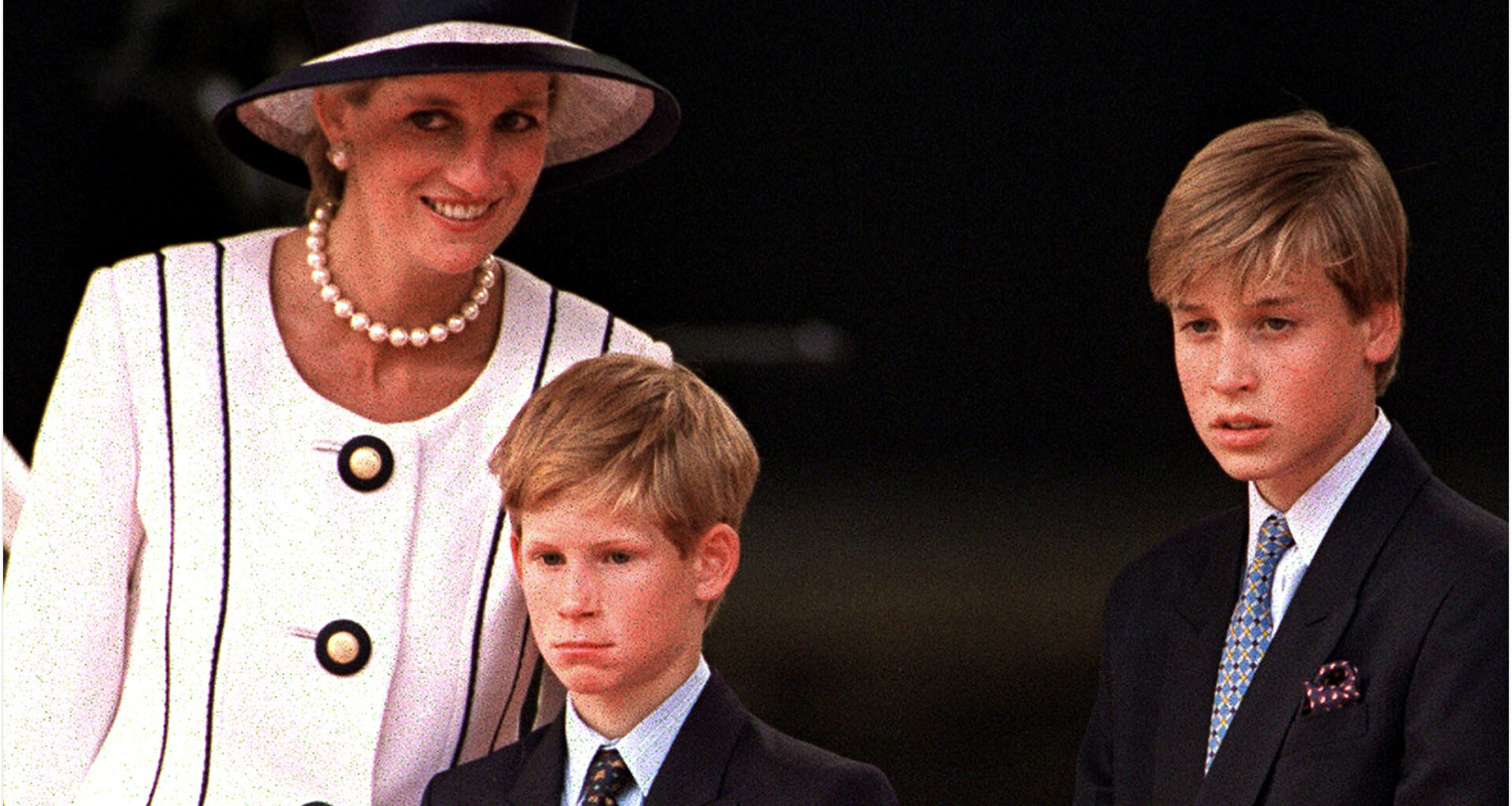 Princess Diana wears a white suit and matching hat with black piping, and poses with her sons Prince Harry and Prince William