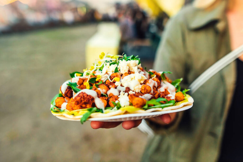 a hand holding out a paper plate piled high with street food
