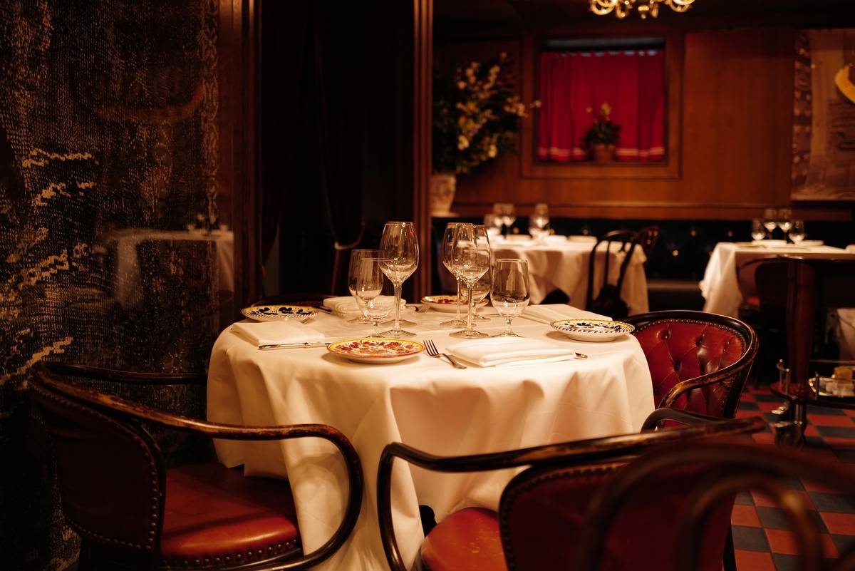 the moody and fancy black and red-hued interiors of the legendary carbone restaurant in new york with white linen tables