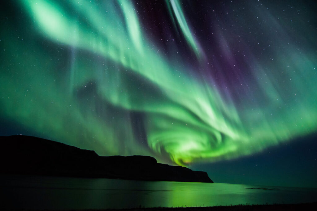 green hued northern lights over lake with mountain in background