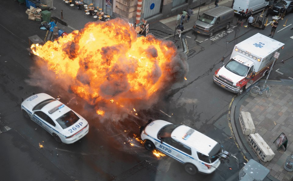 A large explosion on a city street with police cars and an ambulance nearby.