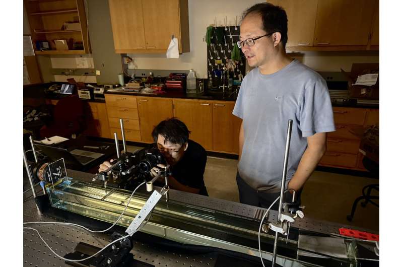 The shape of water can help researchers manipulate how much energy flows through a barrier. Likun Zhang (right) senior scientist at the National Center for Physical Acoustics, and Zhengwu Wang, a doctoral student in physics, take photos of the water passing through a barrier while manipulating the angle of the water's meniscus, the curve caused by surface tension near barriers. Credit: Clara Turnage/University Marketing and Communications Tiny waves, big impact: Study finds new way to control fluid in space
