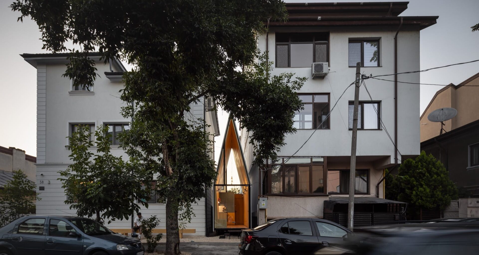 a tiny, contemporary cafe with a steep, pointed roof sits between two larger conventional buildings, designed by Vinklu