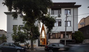a tiny, contemporary cafe with a steep, pointed roof sits between two larger conventional buildings, designed by Vinklu