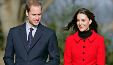 Prince William wears a suit and Kate Middleton wears a bright red coat with black buttons and a black polo neck underneath