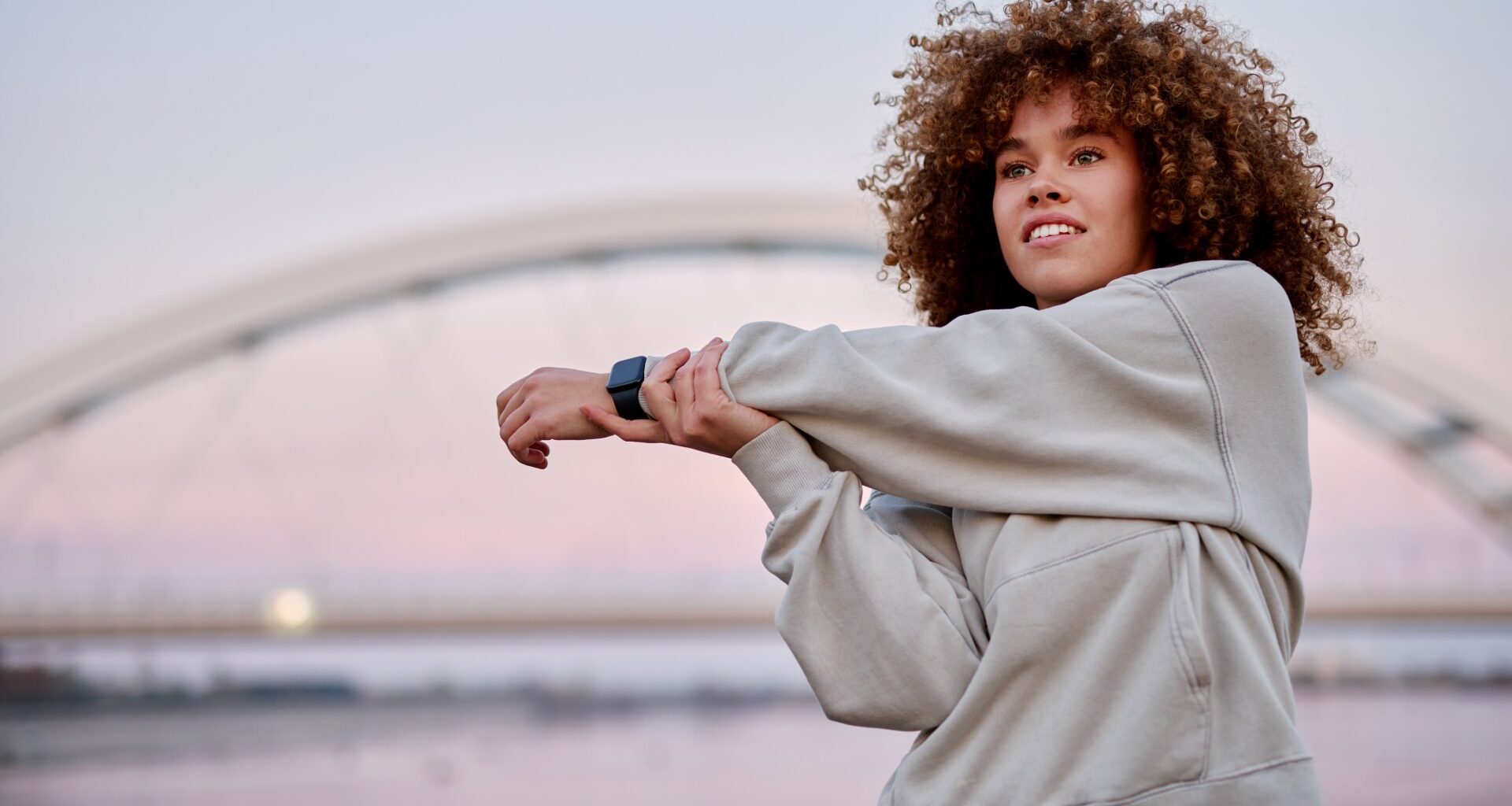 Woman standing outside at sunset stretching her arm across her body