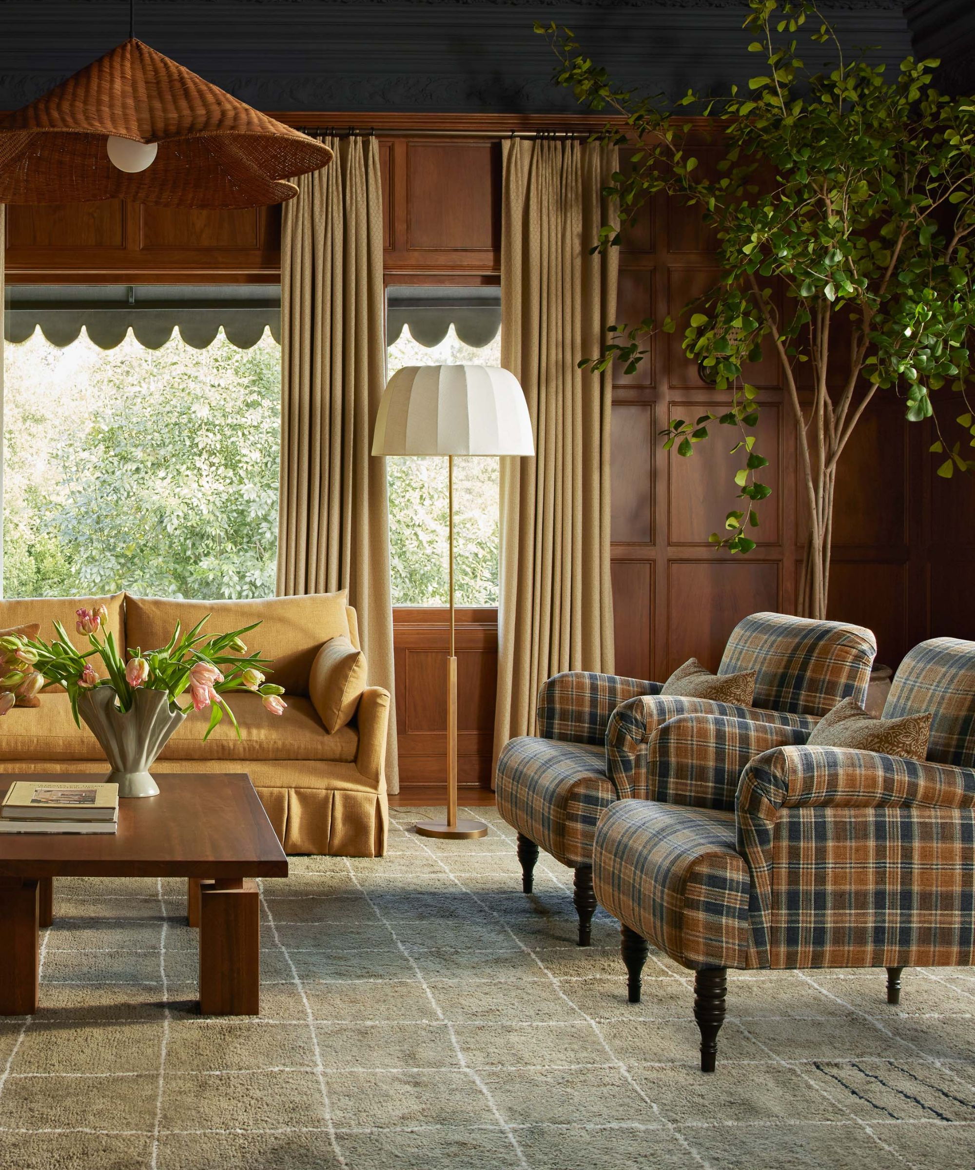 preppy living room with a dark painted ceiling, wooden paneled walls, an earthy green checked rug, deep yellow pleated couch, and two green and ochre plaid arm chairs