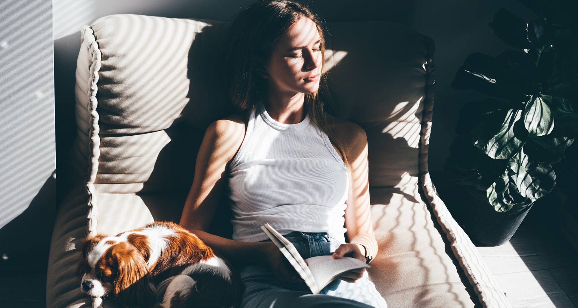 Woman reading a book and cuddling a dog on a sofa.