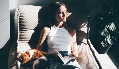 Woman reading a book and cuddling a dog on a sofa.