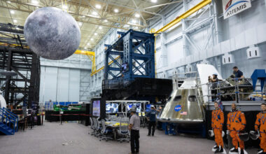 A large inflatable moon hangs over a couple of men below next to cutouts of three astronauts wearing orange jumpsuits