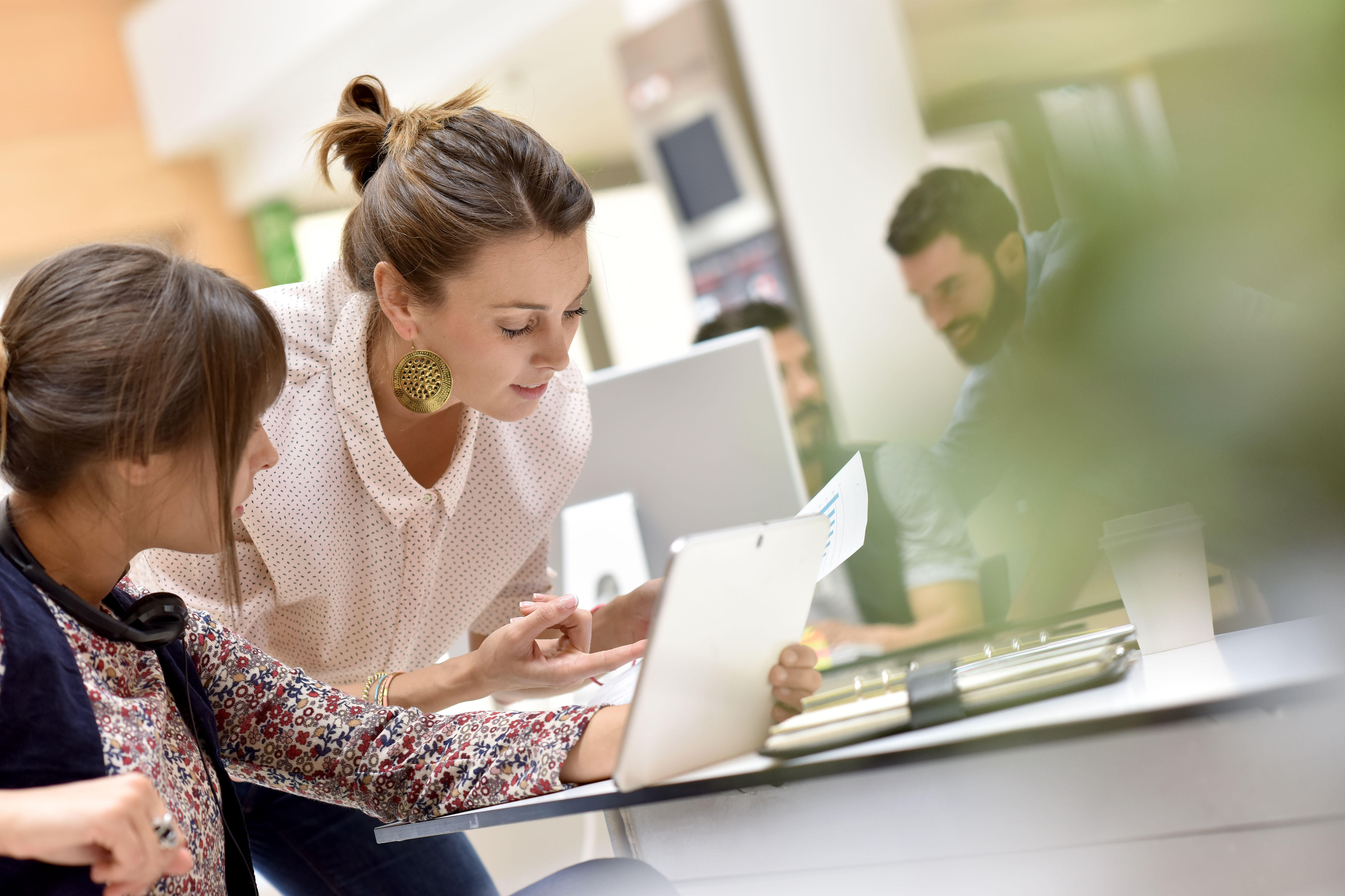 Two businesswomen reviewing documents on a tablet in an office.