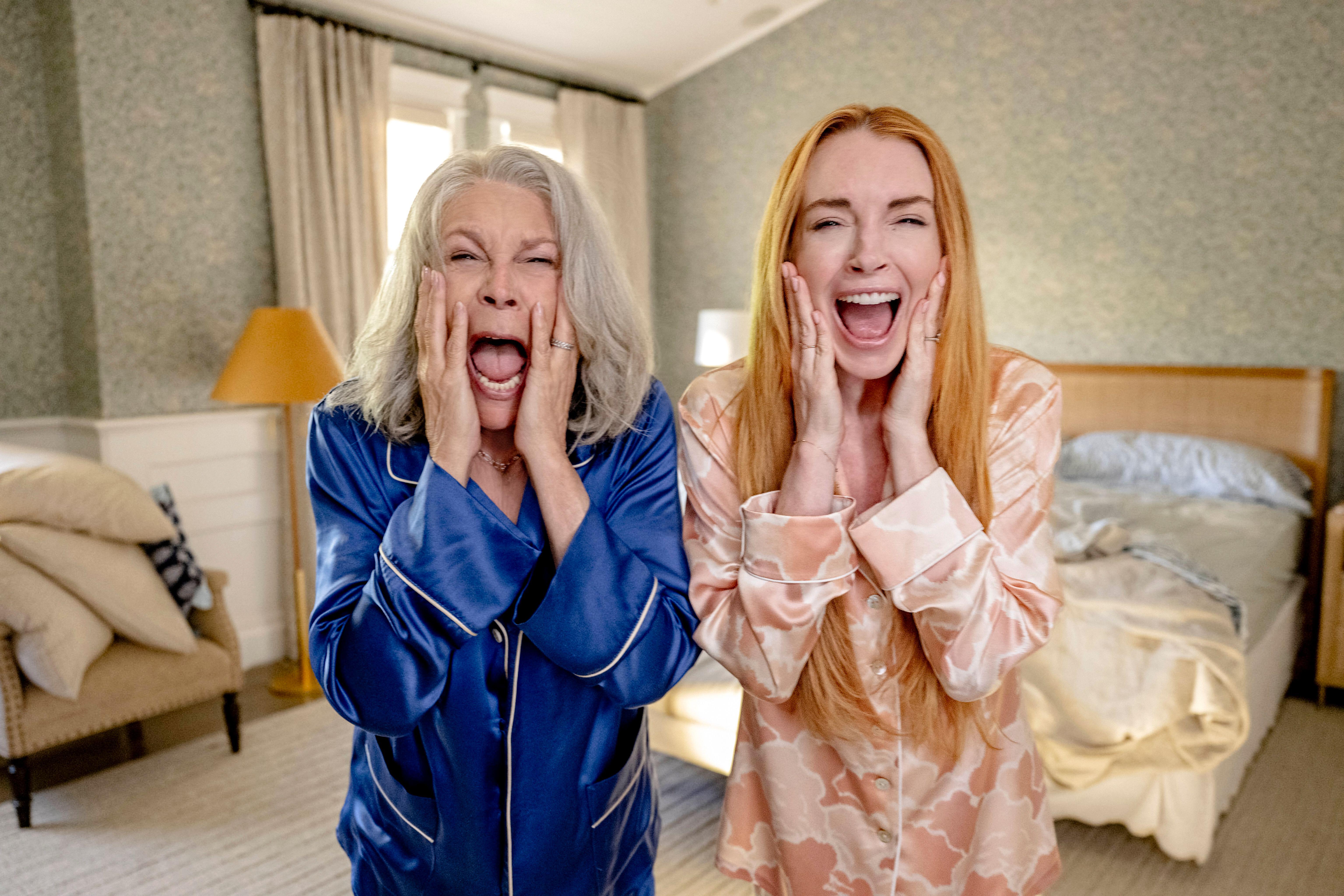 Jamie Lee Curtis and Lindsay Lohan in pajamas, mouths open in surprise.