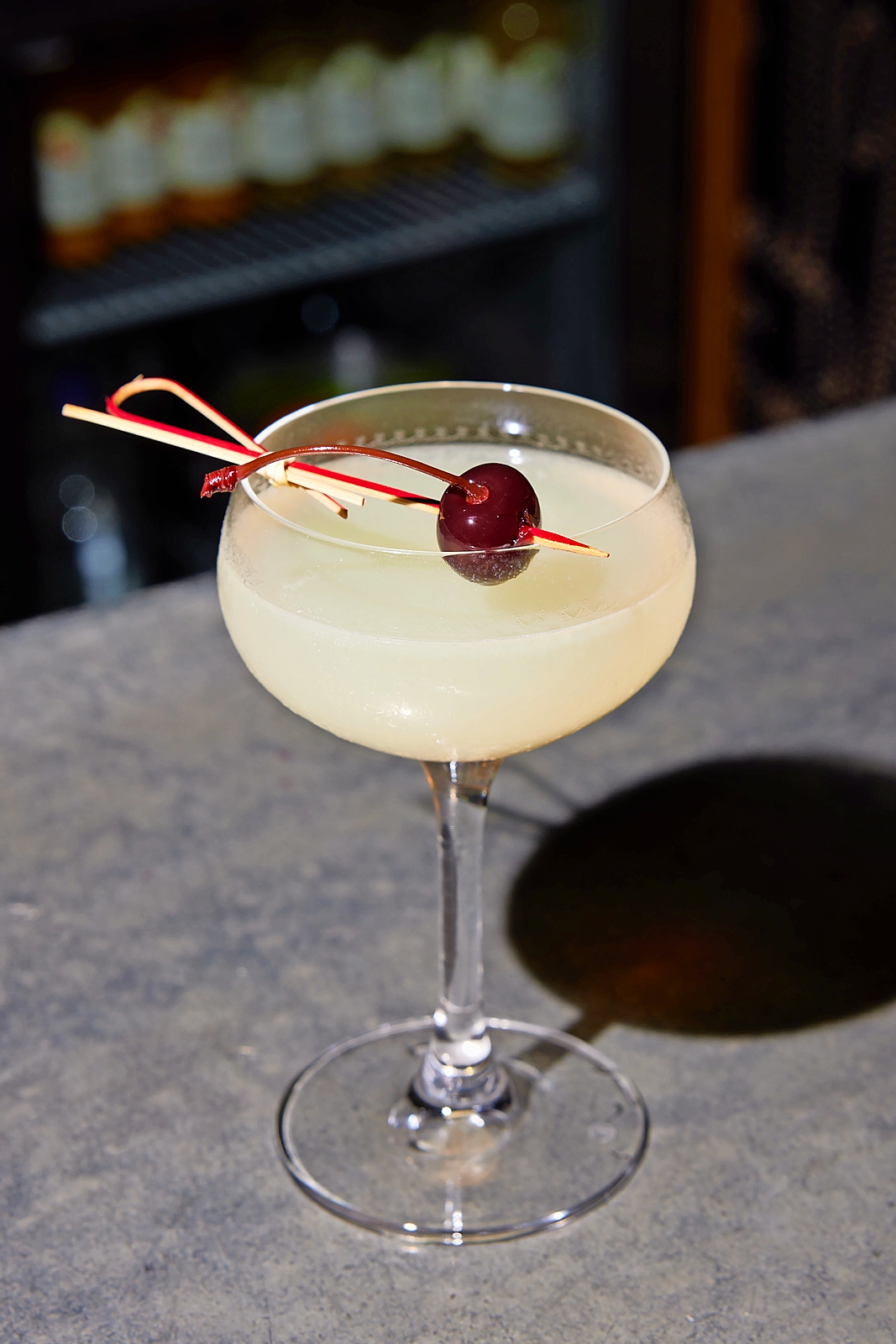 Cocktail in coupe glass garnished with a cherry.