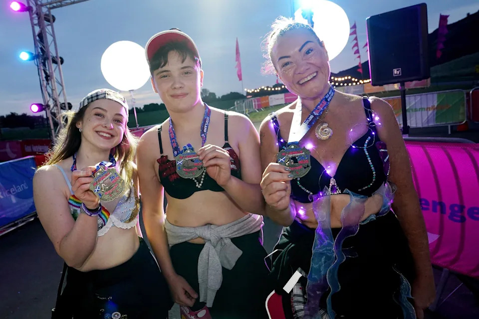 Three walkers in their bras hold up medals, smiling, having completed their challenge