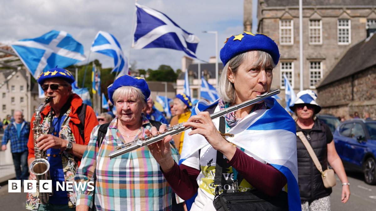 A woman draped in a saltire plays a flute at the front of a crowd of pro-independence marchers