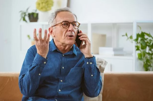 An older man sat on a sofa and speaking into his mobile phone