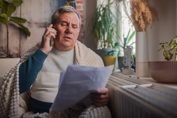 Energy crisis, a man sits next to a cold radiator with a blanket on his back