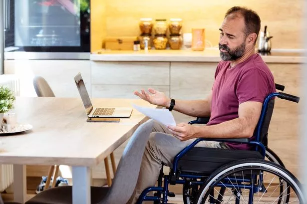 A disabled person in a wheelchair beside a table with a laptop in it. 