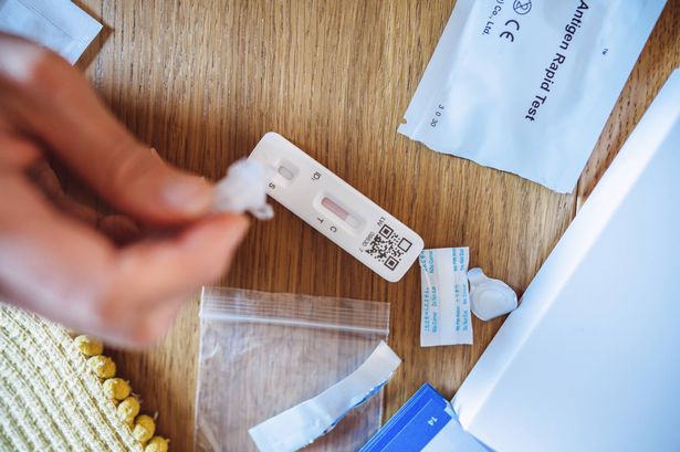 A woman squeezing the sample liquid on a test strip while carrying out a Covid-19 rapid self test at home