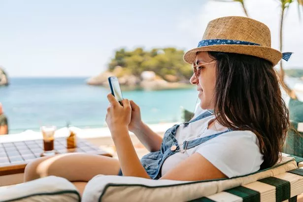 Relaxed young woman using her phone at a seaside café in Parga, Greece.