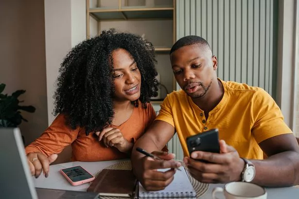 Couple sit at table with laptop and phones booking holiday