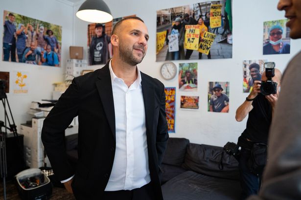 A man in a dark jacket and white shirt mid-conversation