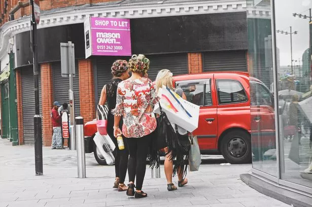 Three people walk through Liverpool City Centre with rollers in their hair, carrying shopping bags