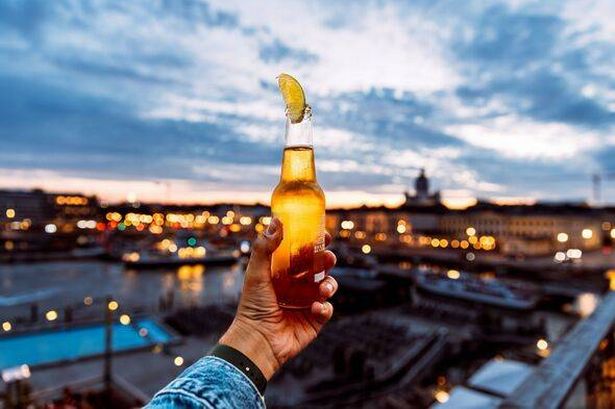 Man holding bottle of beer with lime at sunset