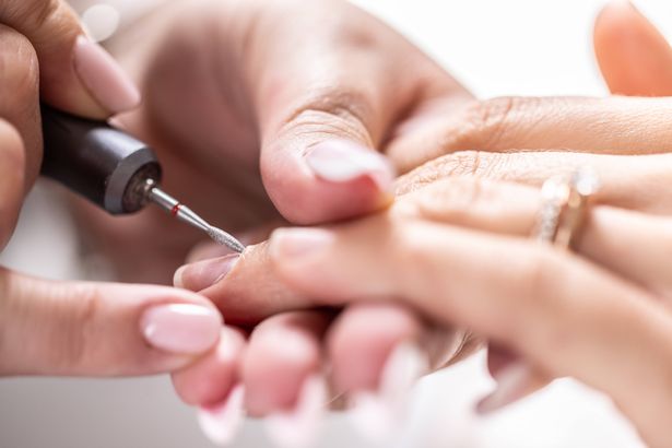Manicurist sanding the skin around the nails with a grinder in a nail salon