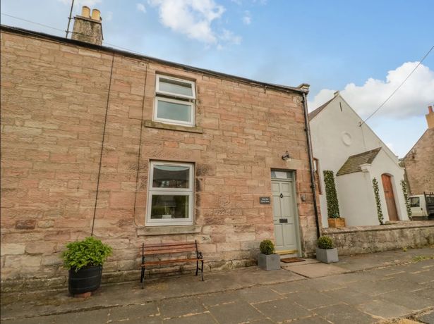 A two-storey old brick cottage on a terraced street.