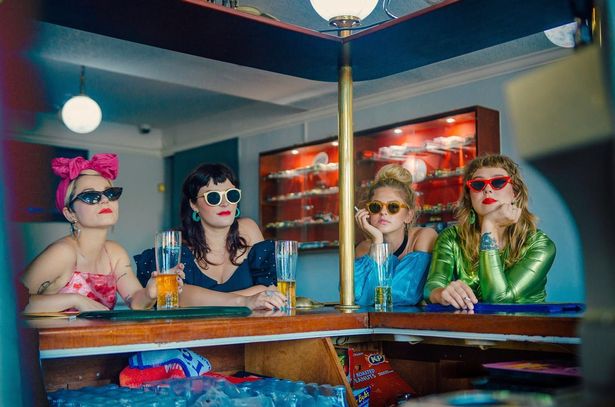 Four women sitting at a table wearing sunglasses and bright clothing