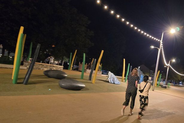people walk along lit up path at night