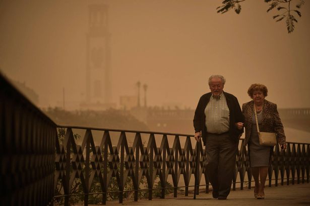 A couple walk across a bridge in a cloud of red dust in Santa Cruz de Tenerife, Spain