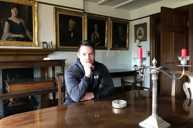 A picture of Jordan Adlard Rogers in front of portraits of members of the Rogers family. 